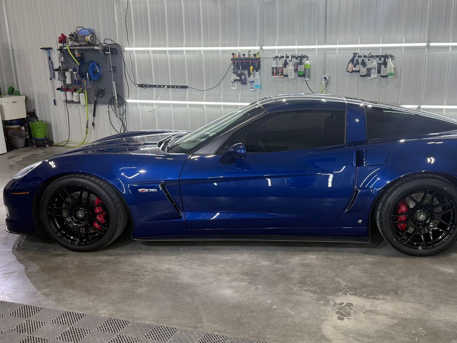 A profile view of a dark blue Chevrolet Corvette parked inside a workshop with equipment mounted on the wall.