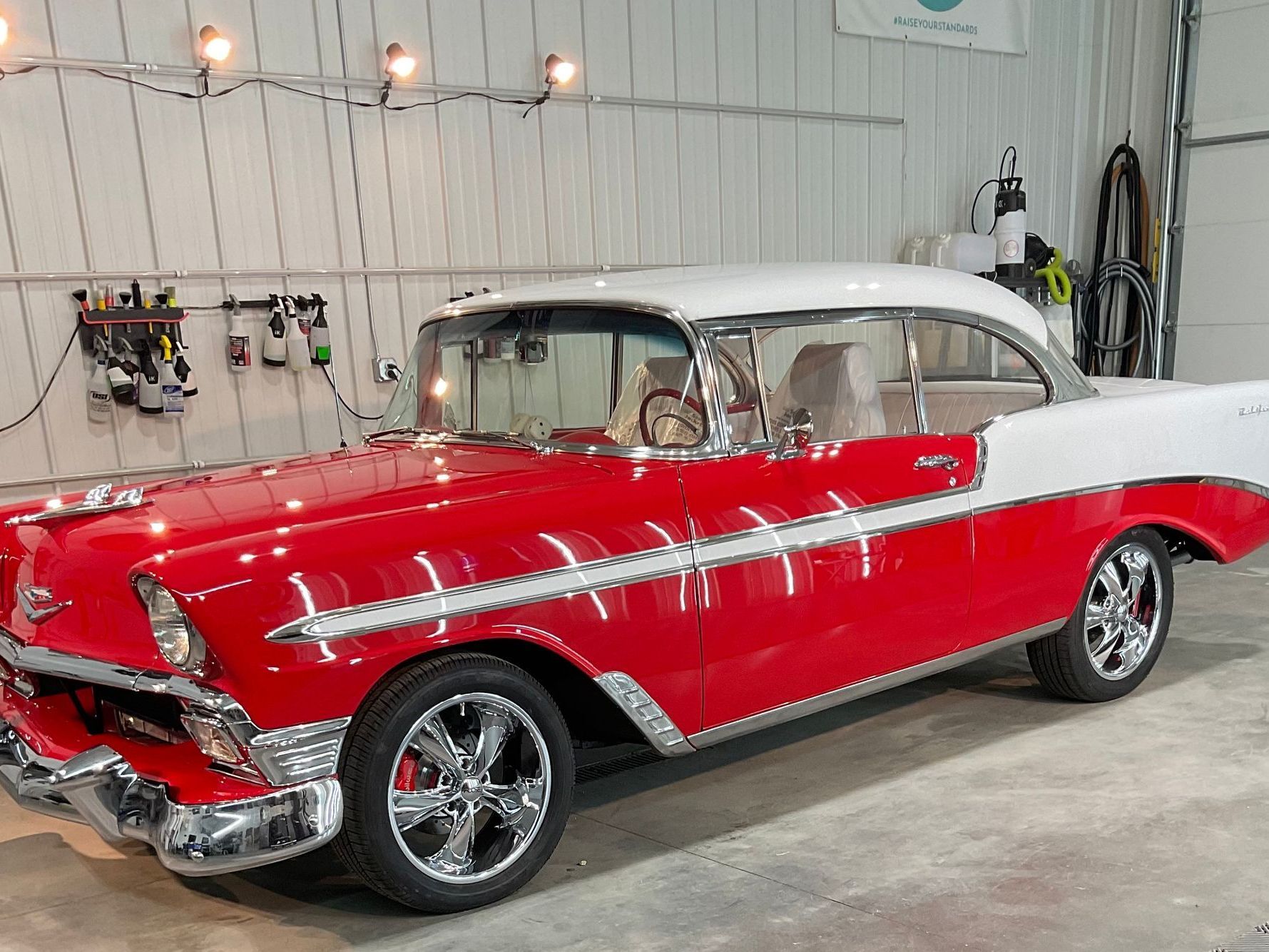 A two-tone red and white classic 1956 Chevrolet Bel Air parked in a garage with chrome wheels.