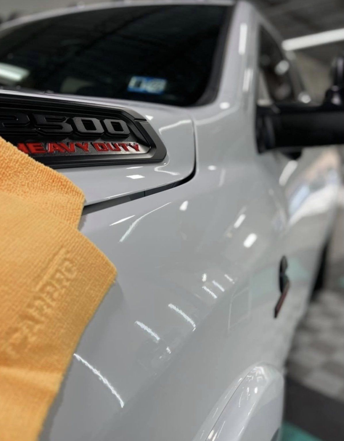 A close-up of a gray RAM 2500 Heavy Duty truck being cleaned with a yellow microfiber cloth.