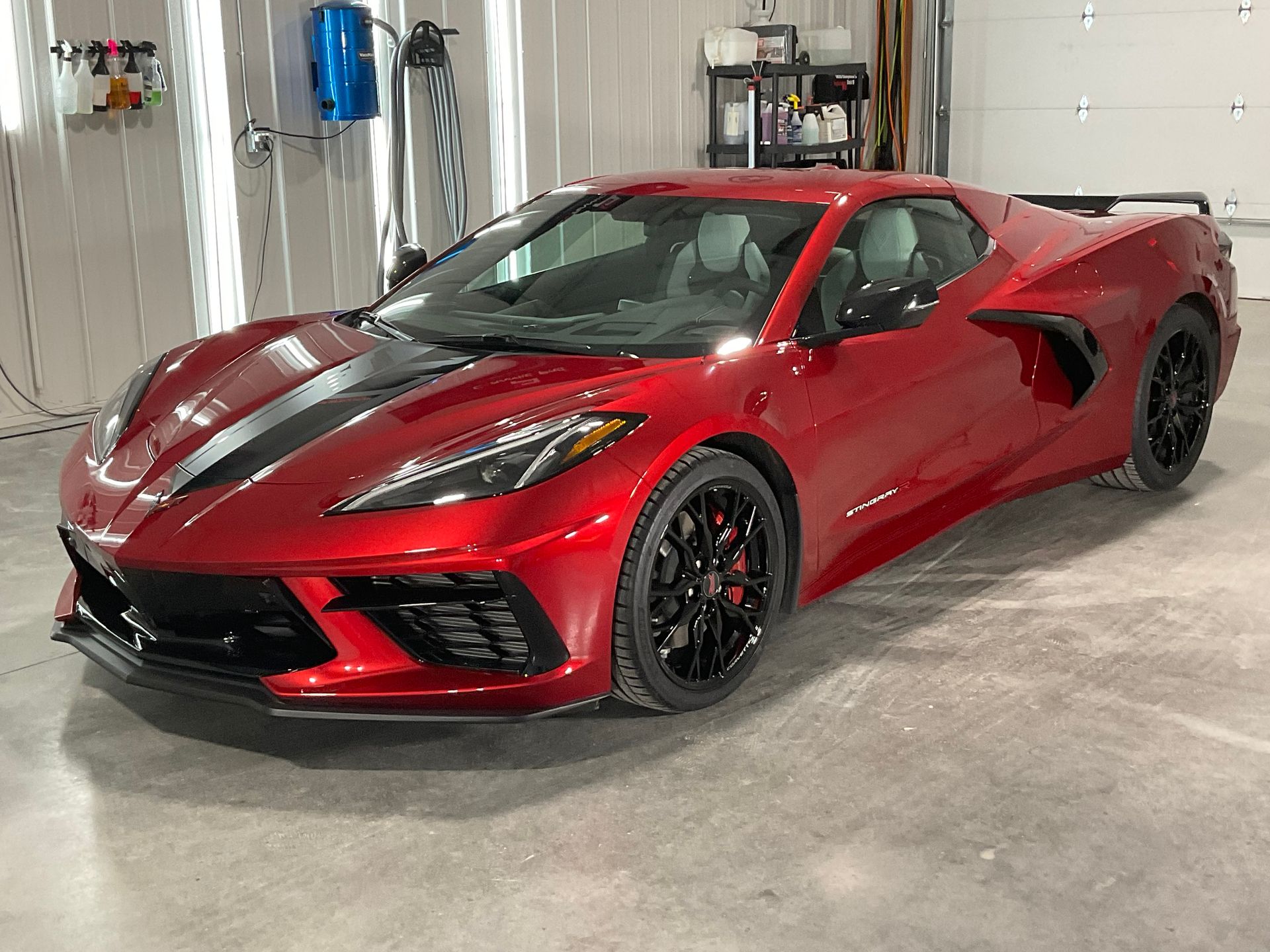 Red sports car with black racing stripes parked in a garage.