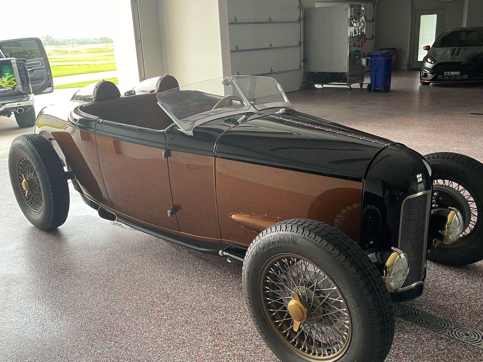 Vintage brown hot rod roadster with yellow wheels parked in a garage