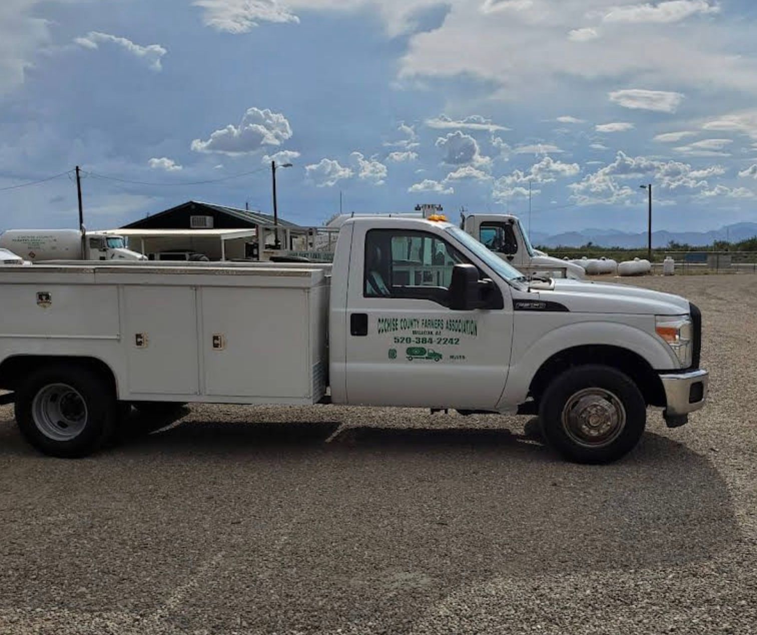 White work truck with storage compartments parked on gravel; cloudy sky backdrop.