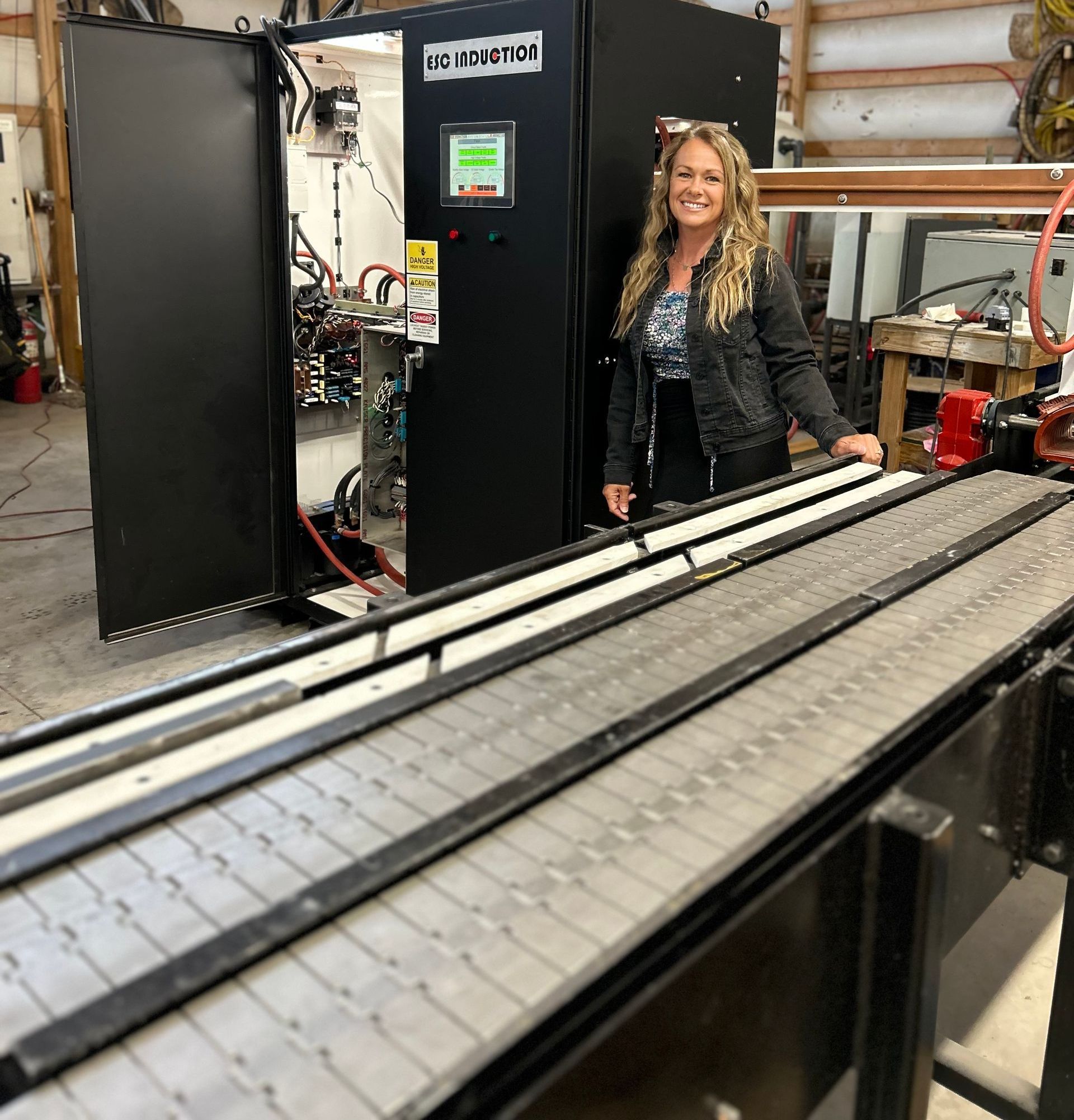 A person stands next to an open industrial control cabinet and a ESC automation line