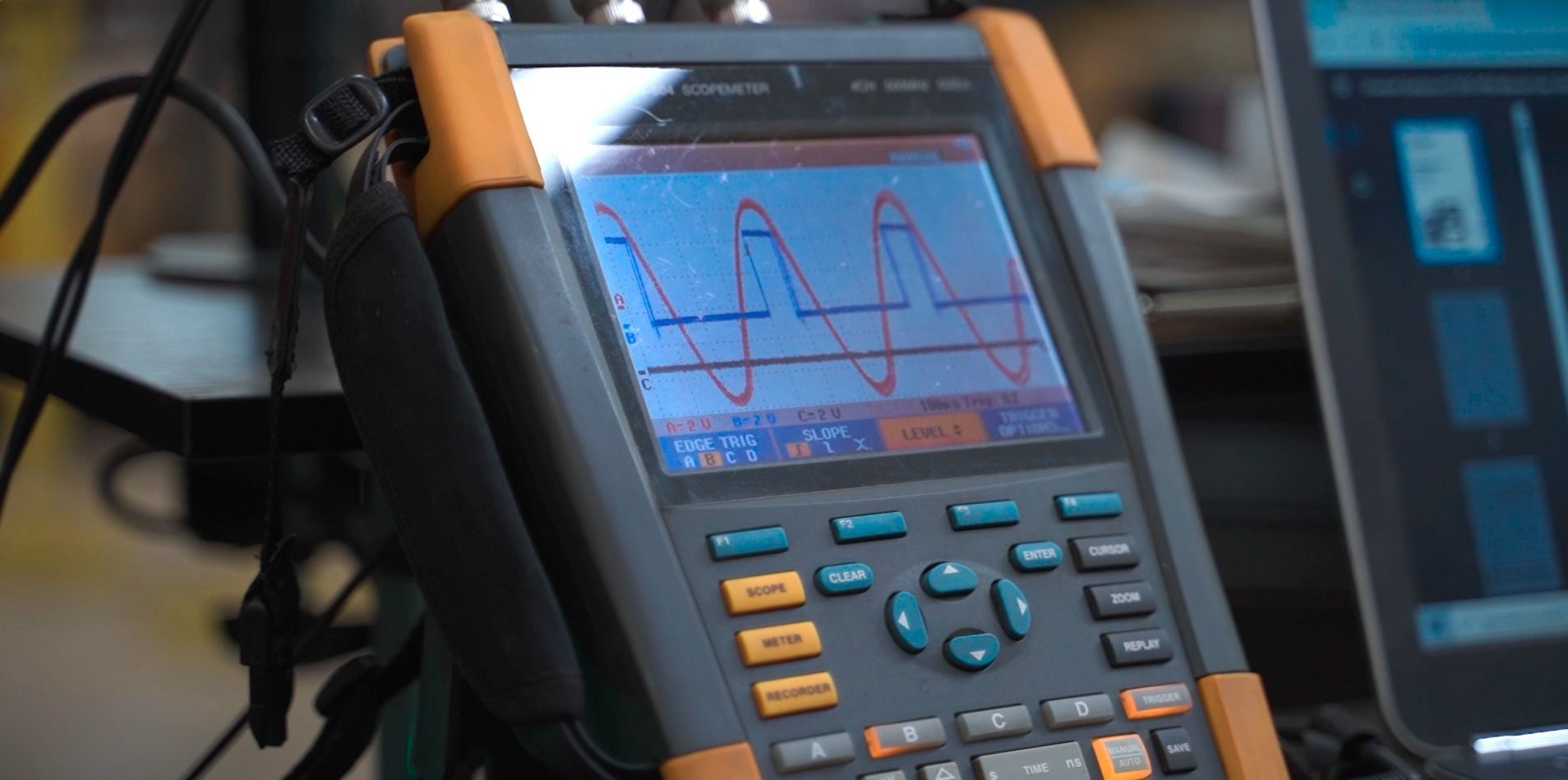A handheld Fluke oscilloscope displays red and blue waveform patterns on its screen a ESC Induction