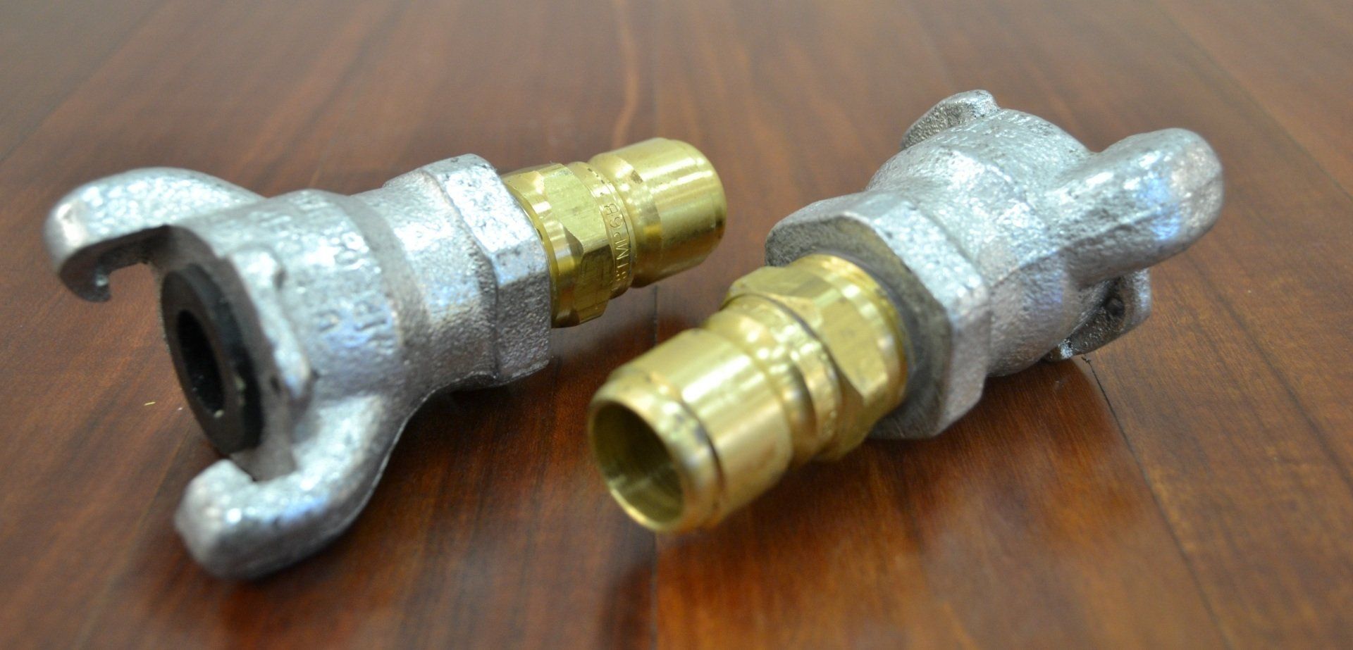 Two metal hose connectors are sitting on a wooden table.