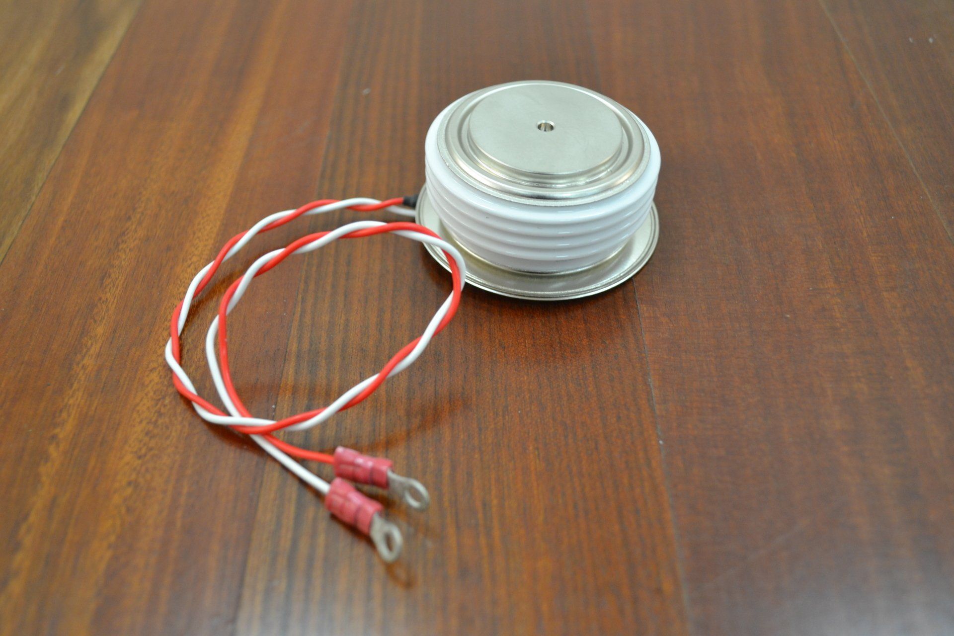 A round object with two wires attached to it is sitting on a wooden table.