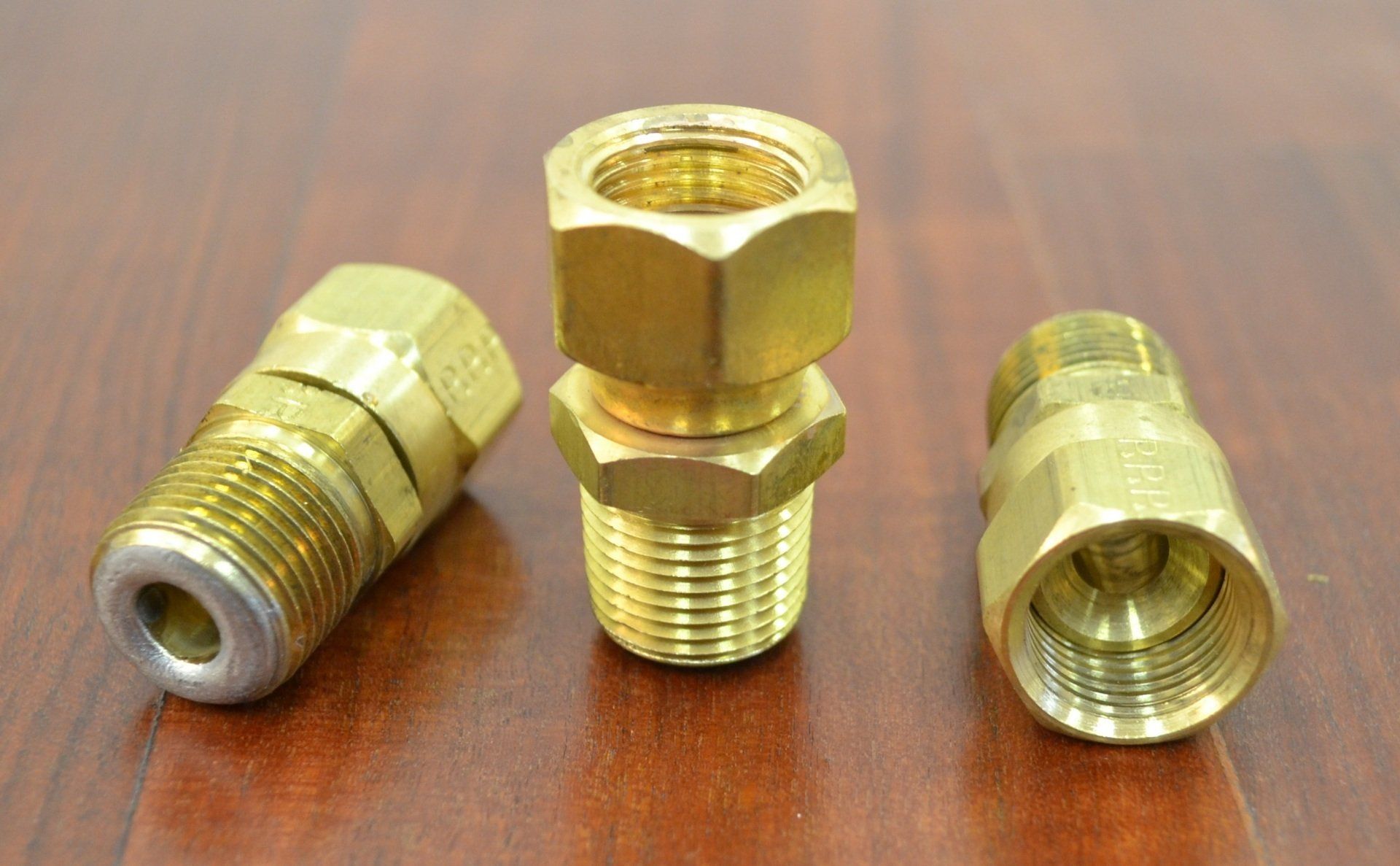 Three brass fittings are sitting on a wooden table.