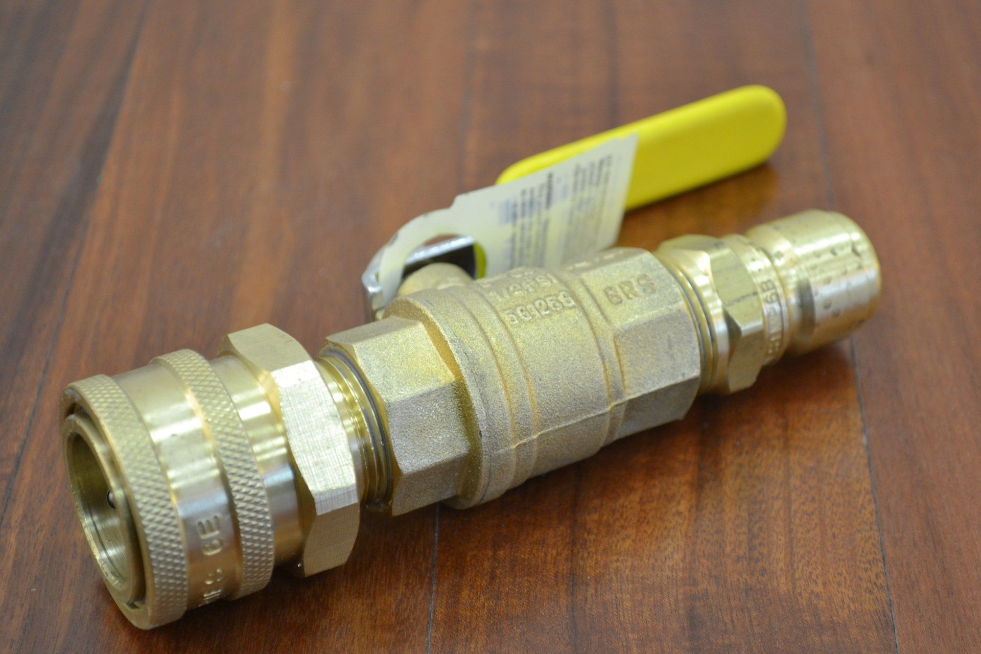 A brass valve with a yellow handle is sitting on a wooden table.
