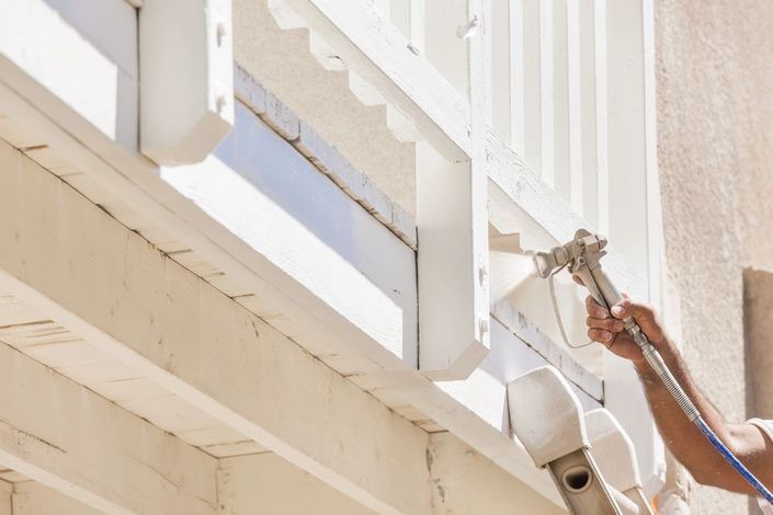 Una persona sta verniciando con vernice spray bianca la ringhiera di un balcone sulla facciata di un edificio.