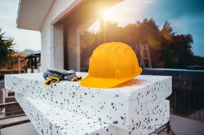 Casco giallo e guanti da lavoro su una sporgenza di pietra all'esterno di un edificio moderno al tramonto.
