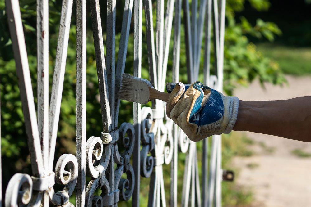Mano guantata che dipinge una recinzione di metallo bianco con un pennello all'aperto