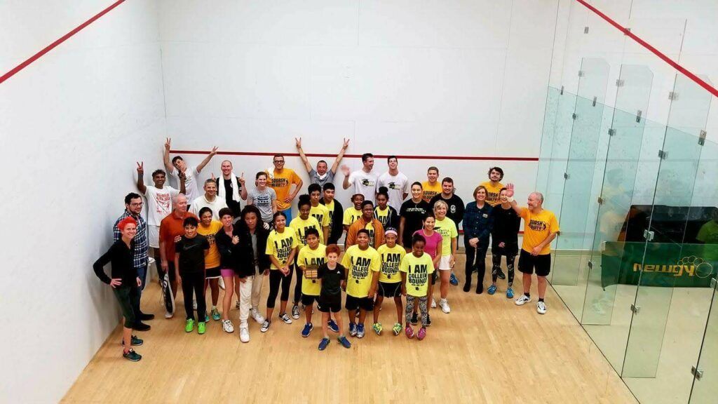 A group of people are posing for a picture on a squash court.