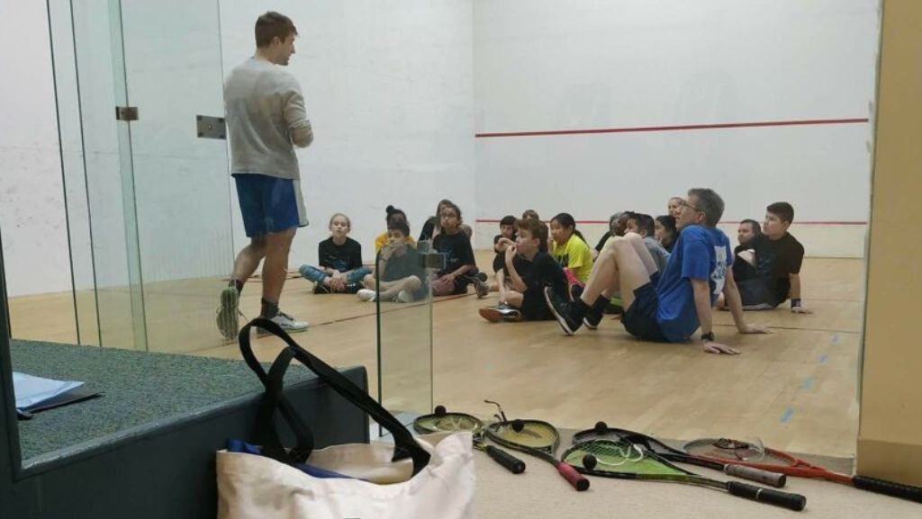 A man is standing in front of a group of people sitting on the floor.