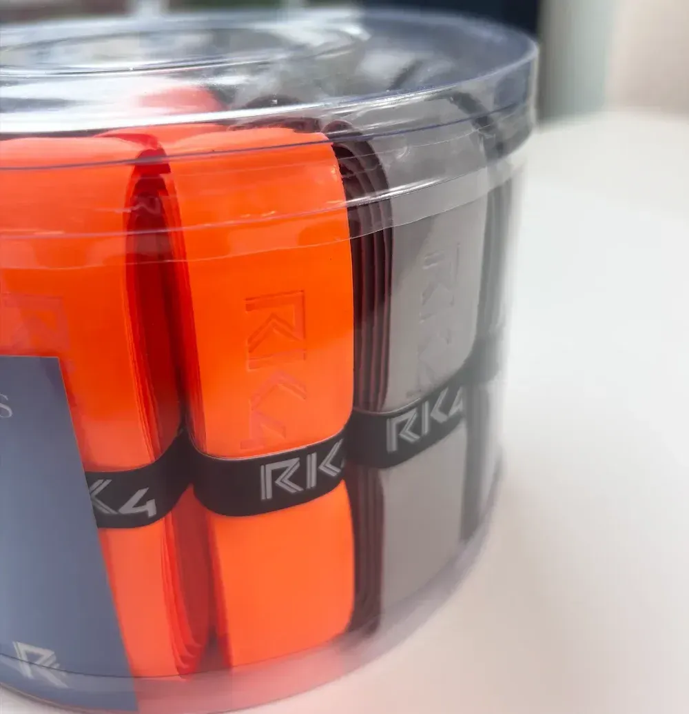 A clear plastic container filled with tennis racket grip tapes of various colors: white, black, gray, and orange.