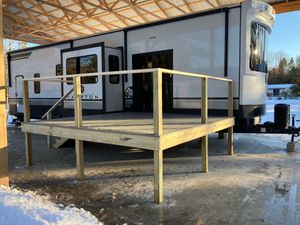 Wooden accessibility ramp with railings outside a white mobile home on a snowy day