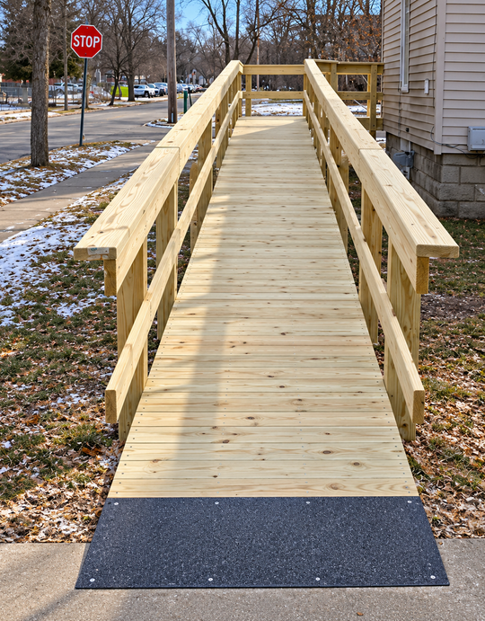 Wooden wheelchair ramp leading to a house with railings and a sloped boardwalk side path