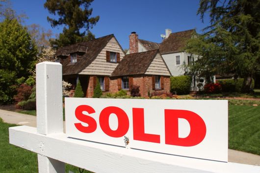 White SOLD real estate sign in front of a suburban house and yard
