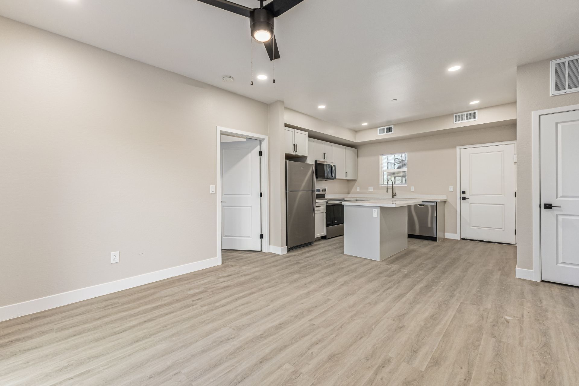 Modern open-concept living room and kitchen with island, stainless steel appliances, and wood-style flooring