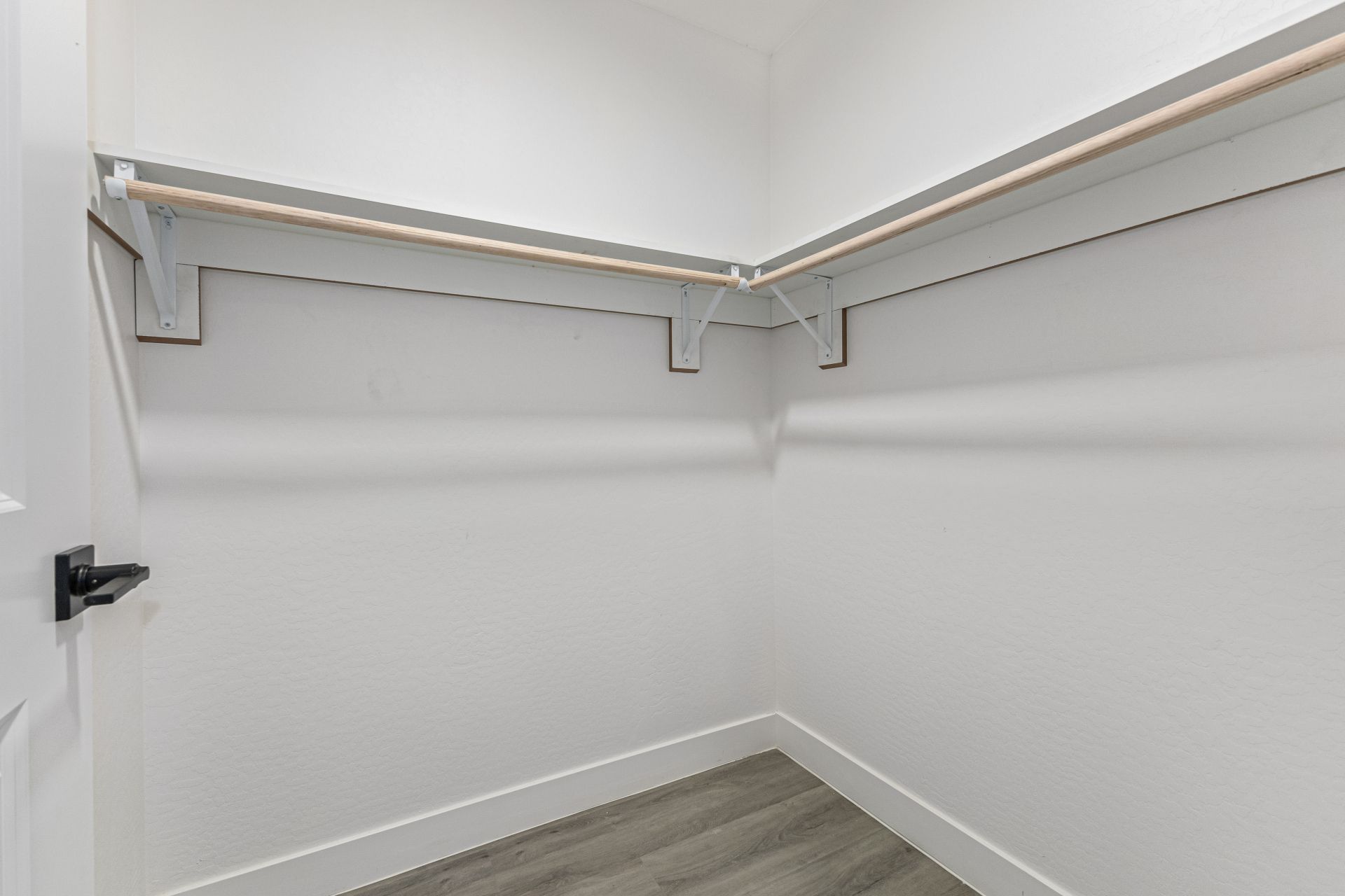 Spacious walk-in closet with white walls, wooden hanging rods, and modern flooring in rental property