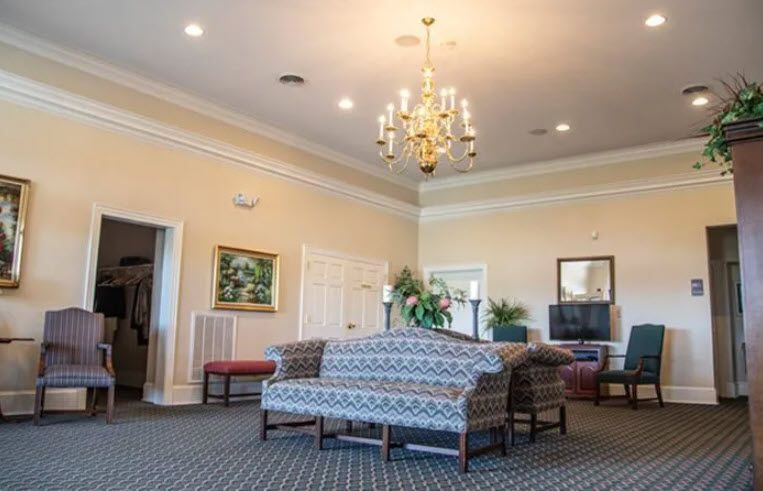 Spacious room with a sofa, chairs, artwork, chandelier, and a TV; neutral colors.