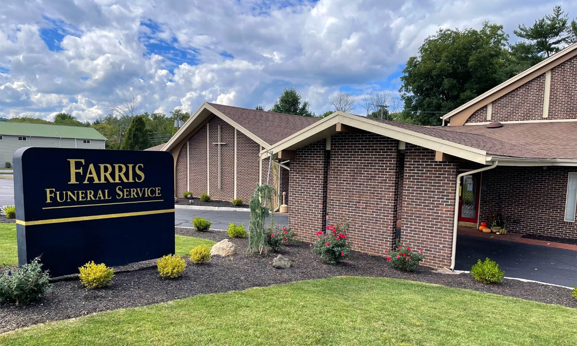 Farris Funeral Service building exterior, brown brick with sign on lawn, cloudy sky background.