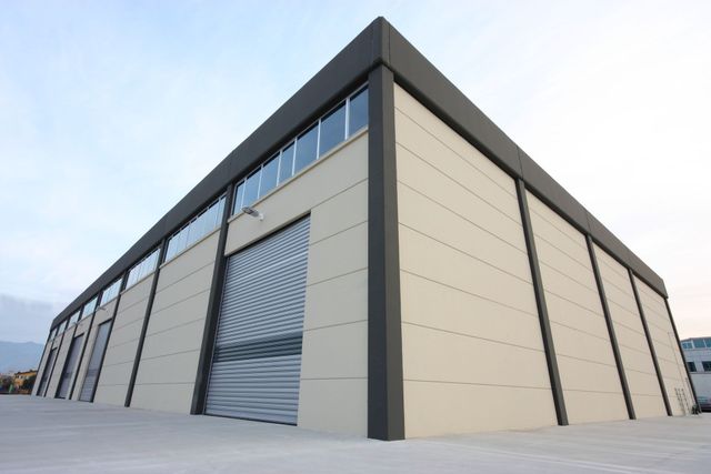 Exterior view of a modern industrial building with a large roller door and windows, in front of a blue sky.