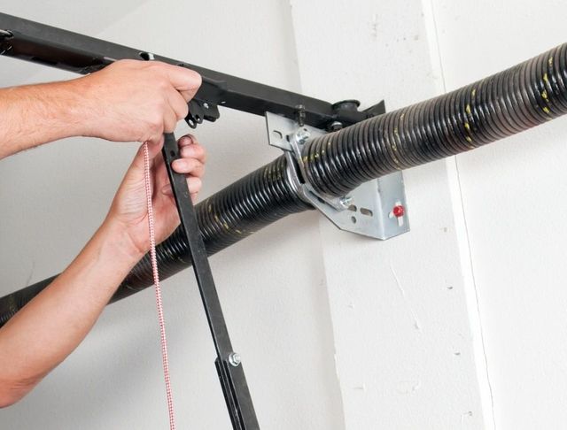Person using tools to adjust a garage door spring system.