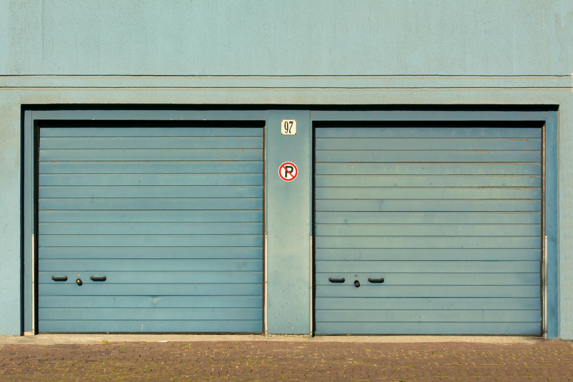 Two blue garage doors in a light blue building, with a small sign between them.