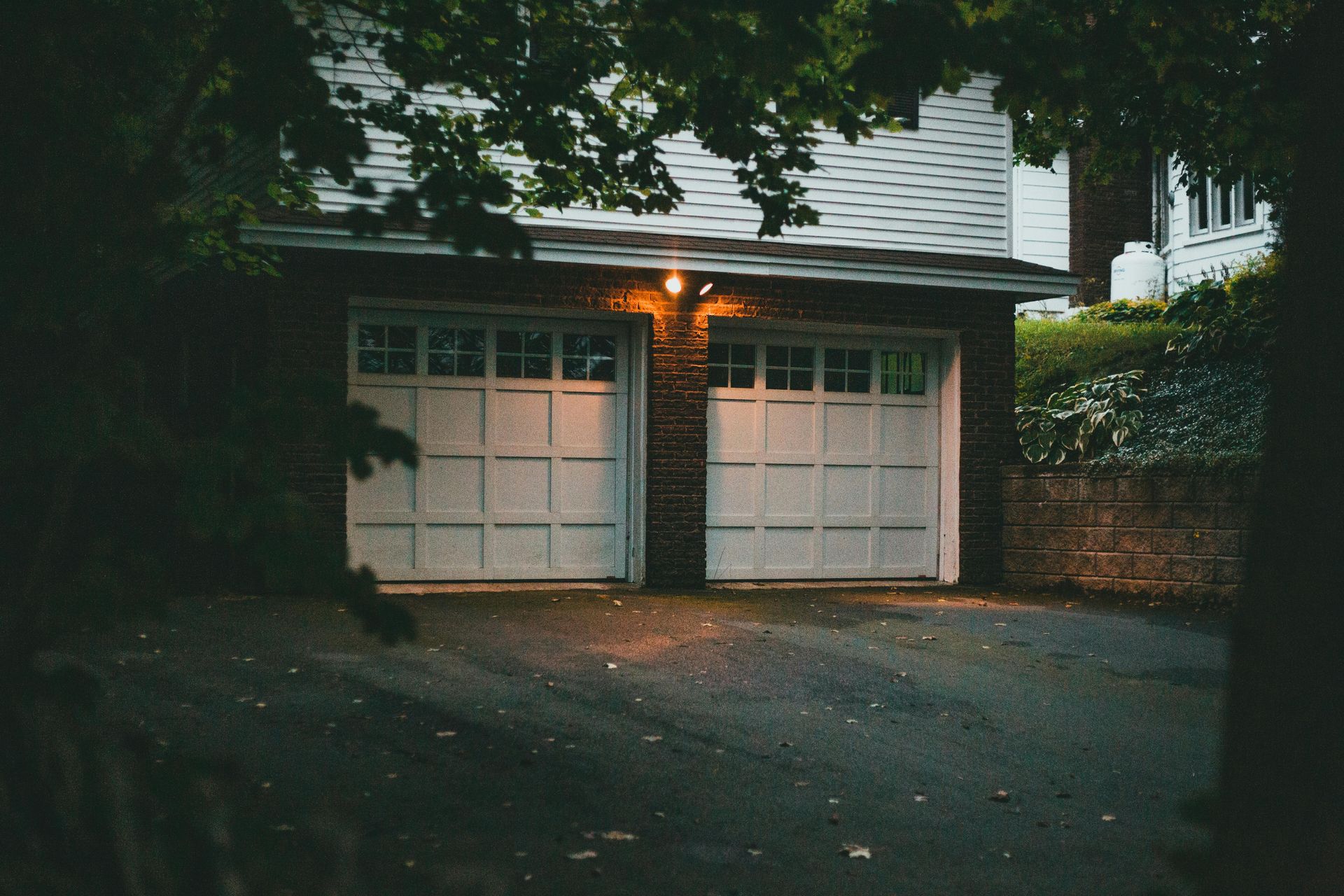 Two-car garage with white doors, lit by a single overhead light. Dark asphalt driveway.