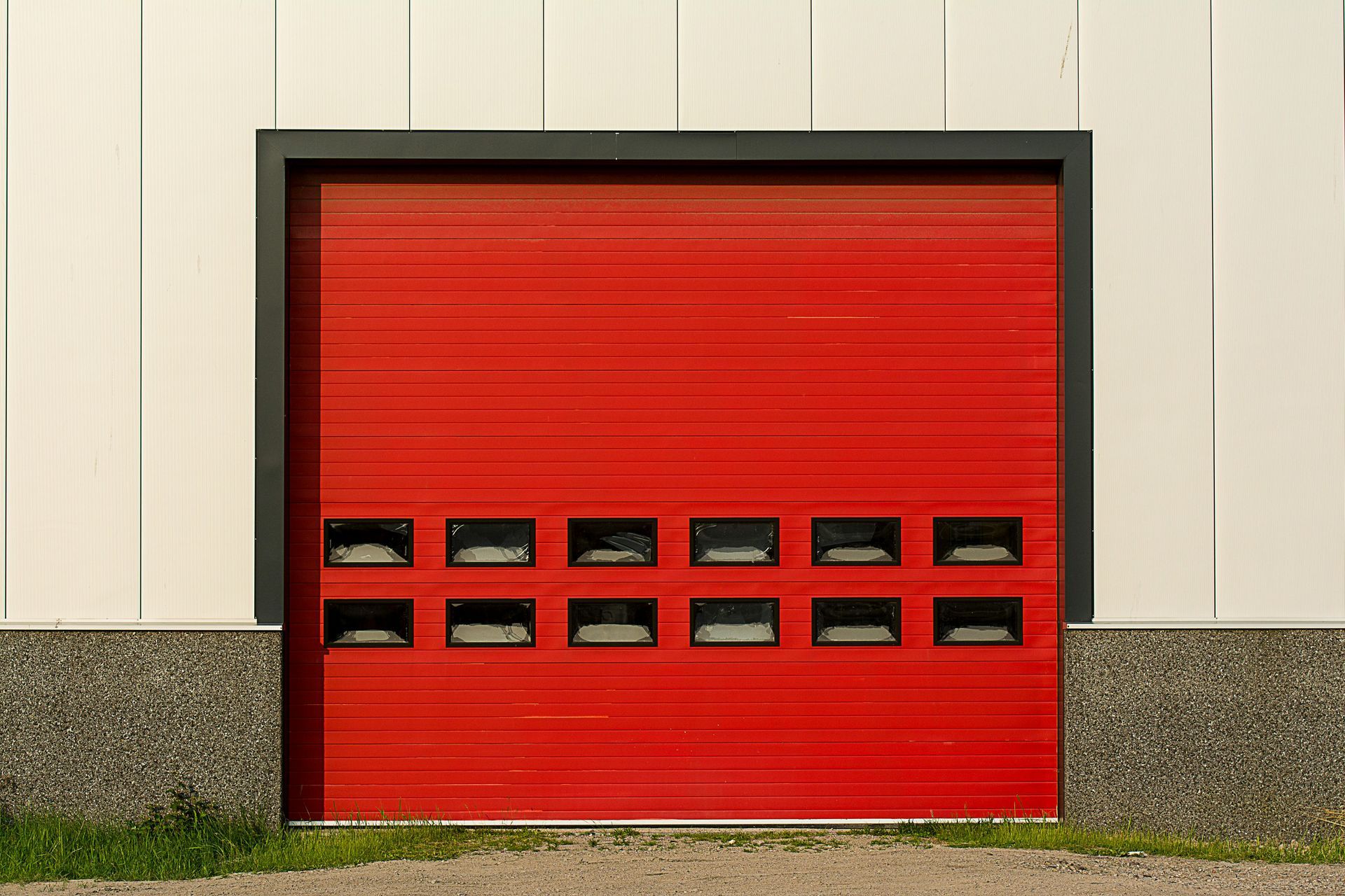 Red industrial garage door with windows, set in a white and gray building.