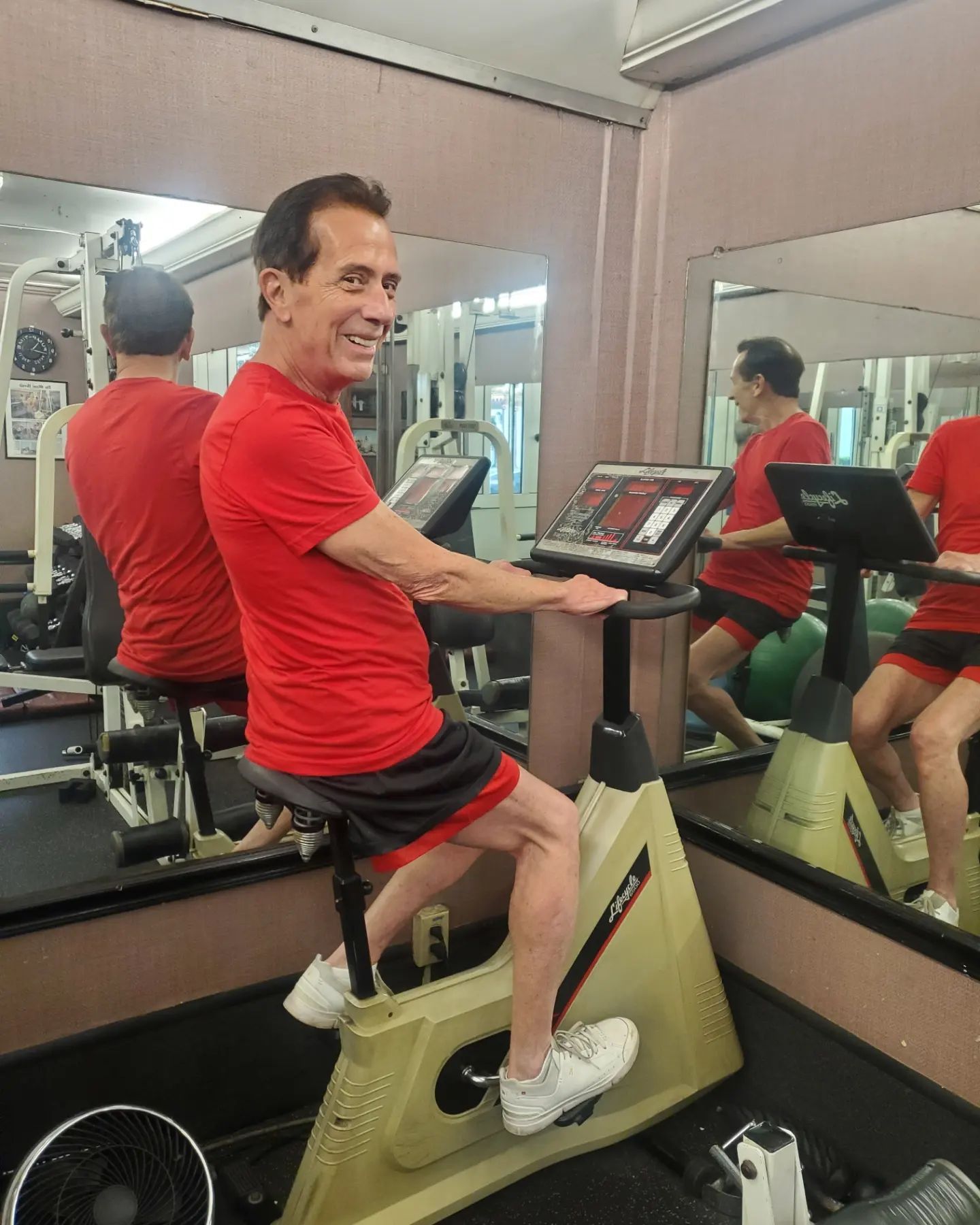 A man in a red shirt is riding a bike in a gym