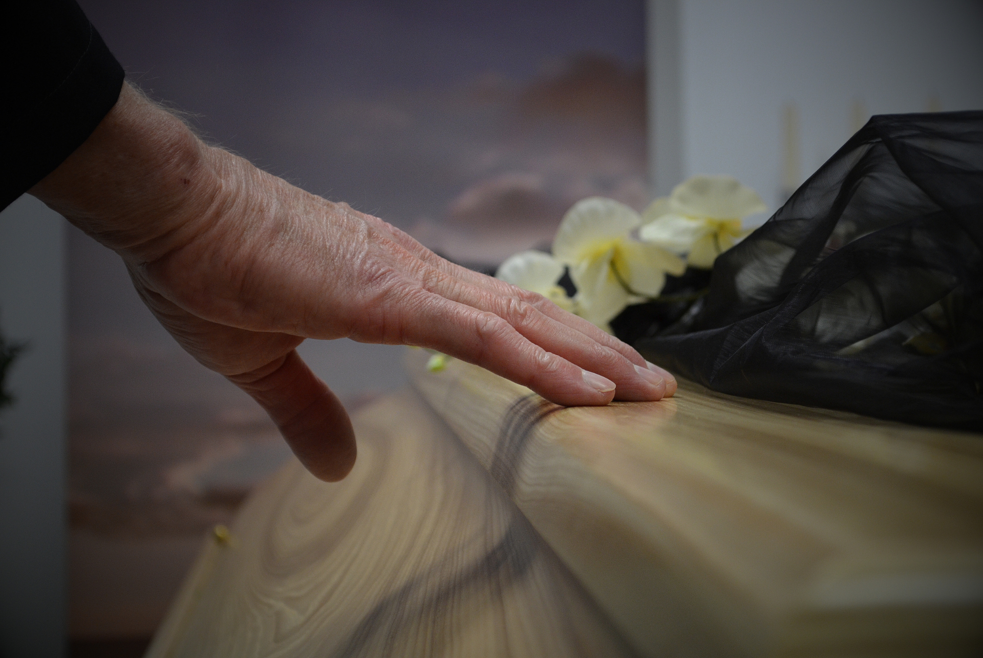 A hand on a casket with flowers on top.