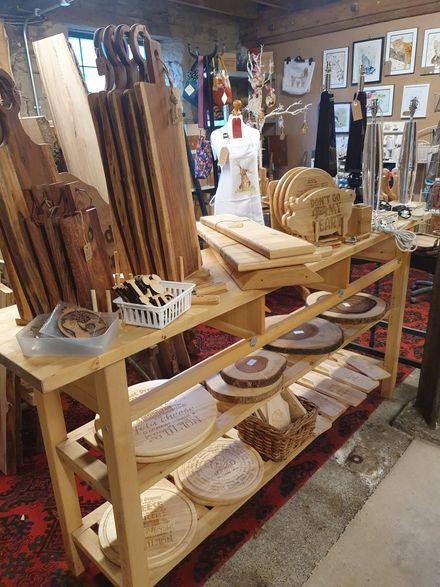 Wooden kitchenware display on shelves in a rustic shop, with bowls, cutting boards, and trays.