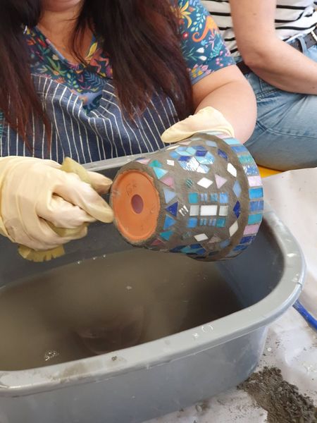 Gloved hands clean a mosaic-covered pottery vase in a basin