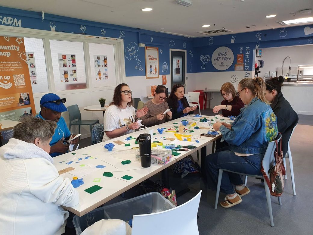 People seated around a table crafting with colorful pieces in a bright classroom or community room