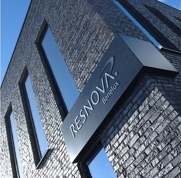 Het logo van Resnova Genk op een modern bakstenen gebouw met hoge ramen, gezien vanaf onderaf.