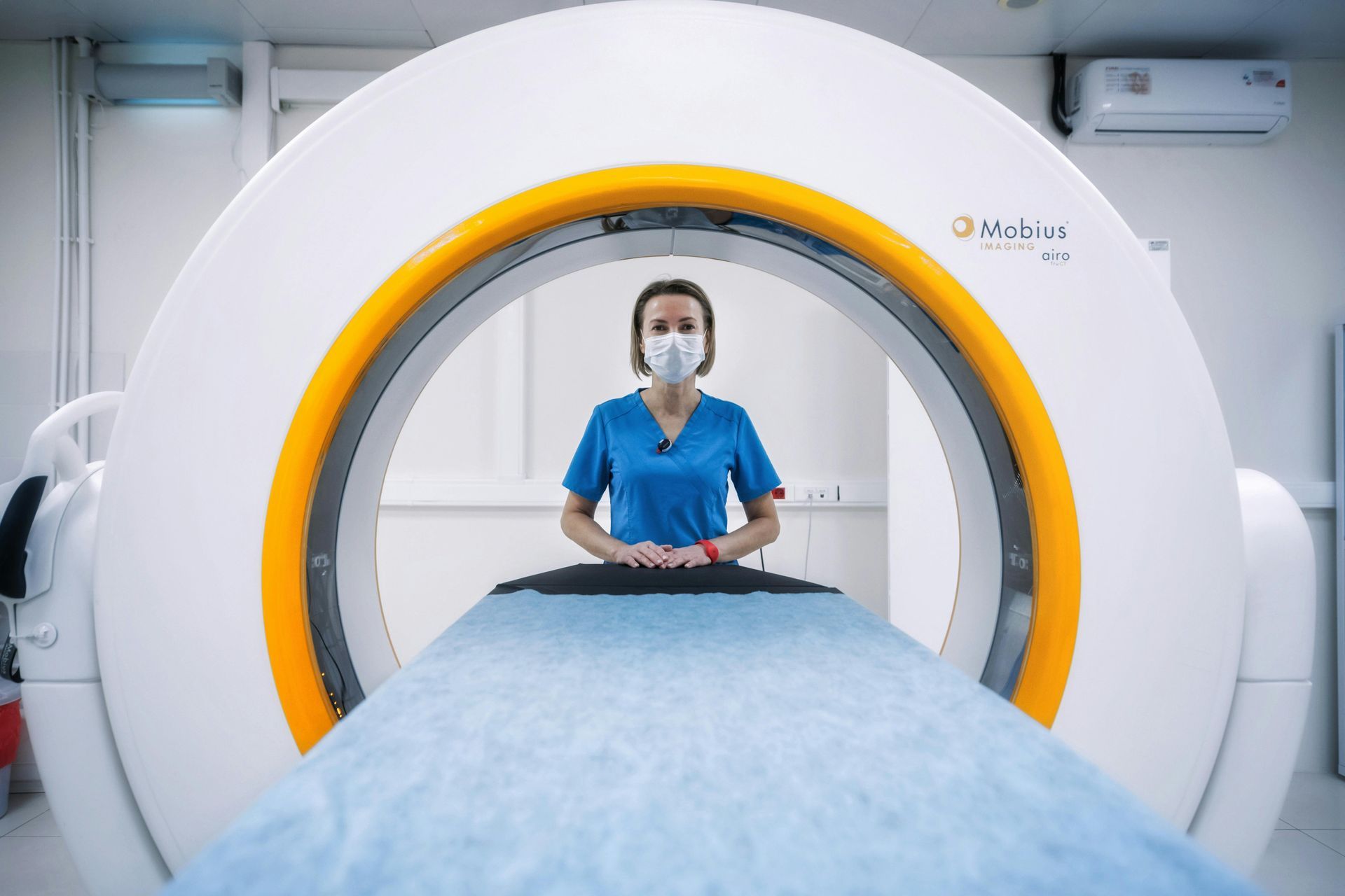 A nurse wearing a mask is standing in front of a ct scan machine.