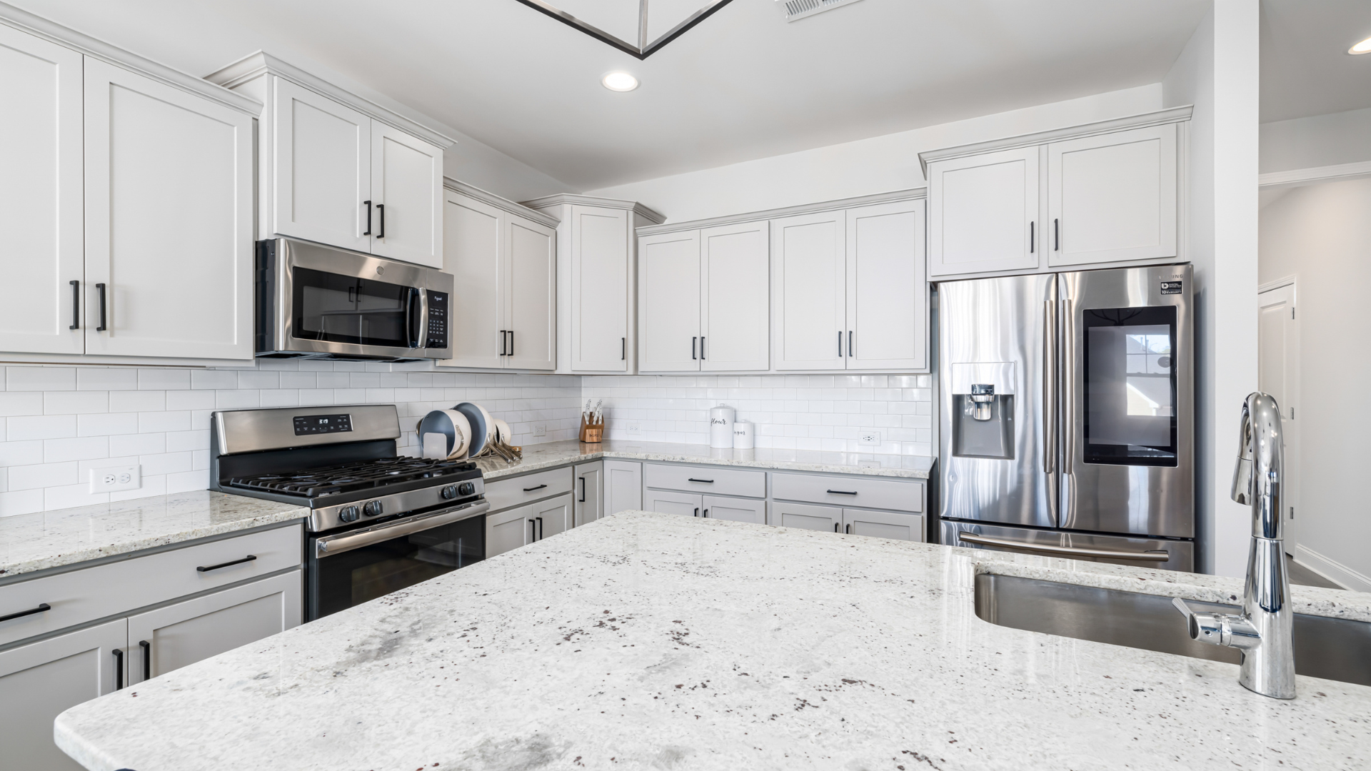 White kitchen with stainless steel appliances, granite countertops, and light fixtures.
