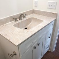 A bathroom sink with a granite counter top and white cabinets.