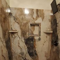 A bathroom with marble walls , shelves , and a shower head.