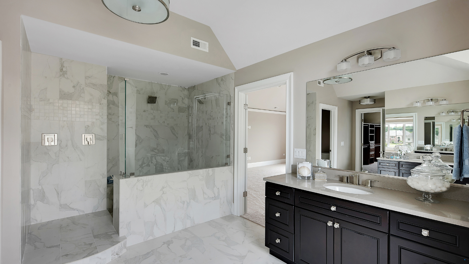 Modern bathroom with marble shower, vanity with black cabinets, and large mirror.