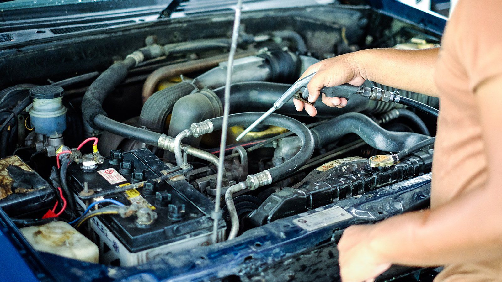 Persona che controlla il motore di un'auto con un'astina di livello; auto blu, cofano aperto.