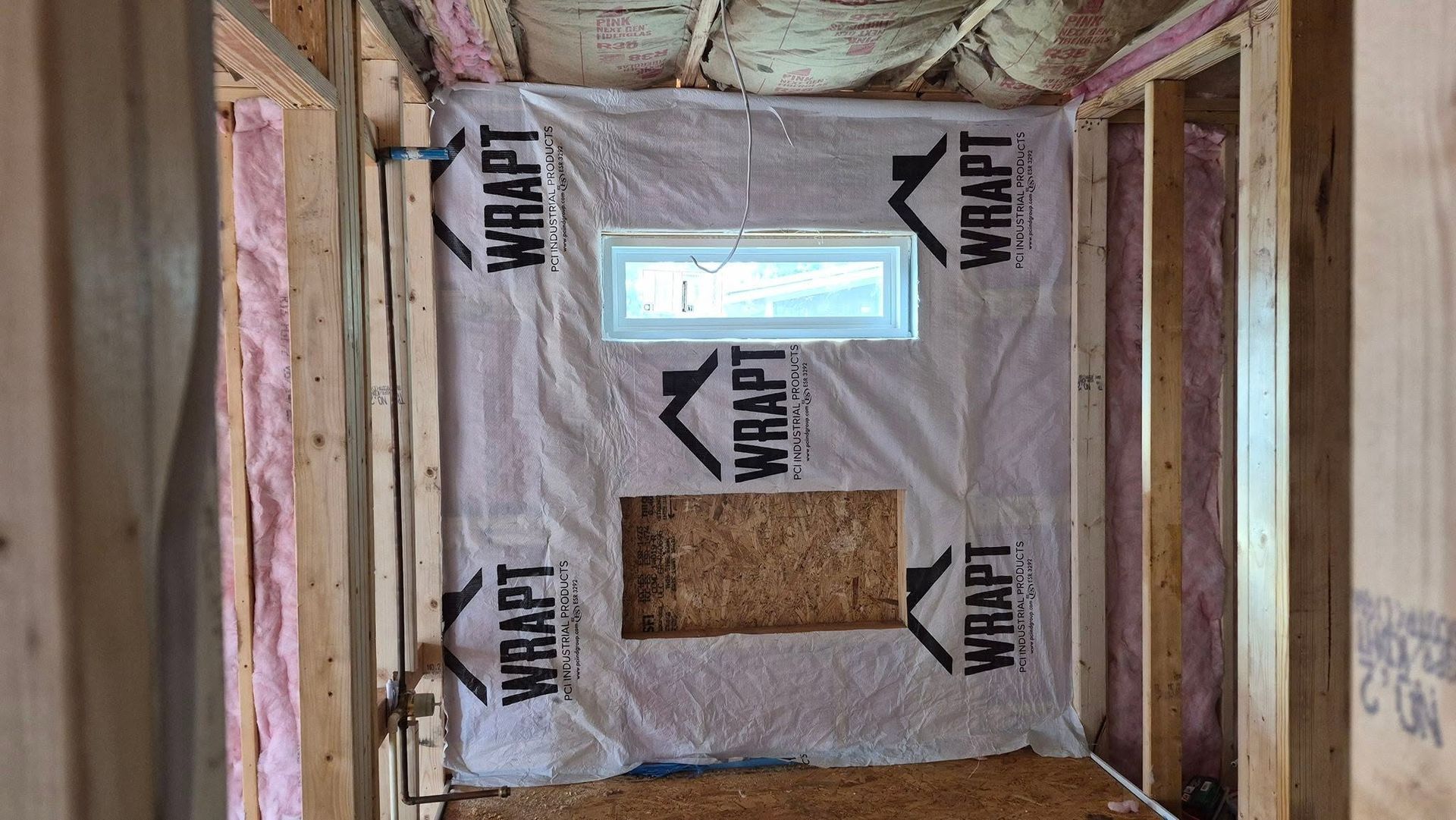 Insulated wall framing with a small window opening and cutout in a construction site