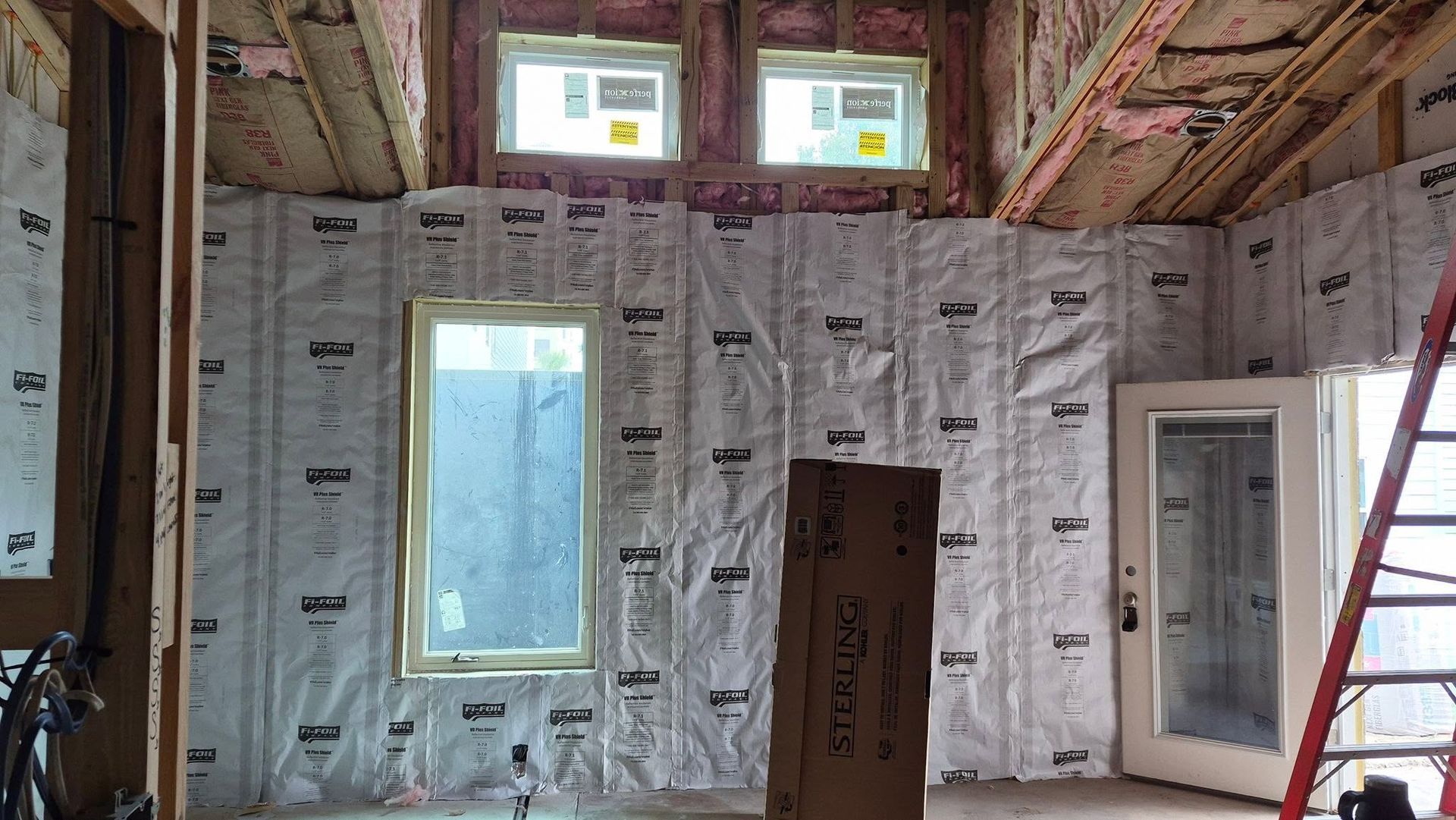 Insulated interior wall under construction with windows, door opening, exposed ceiling, and ladder on the right.