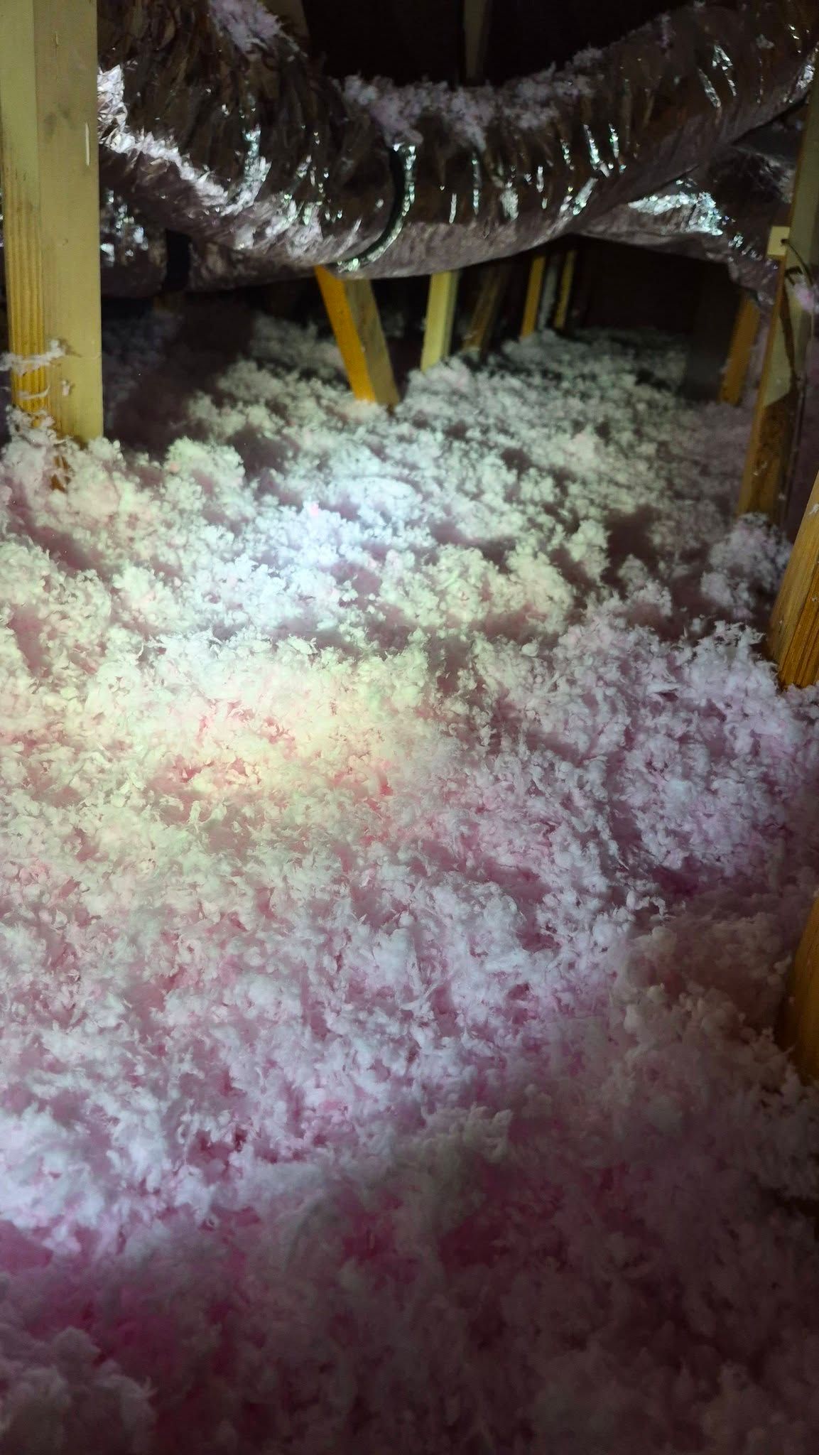 Insulated attic crawlspace with yellow supports and loose white and pink insulation on the floor