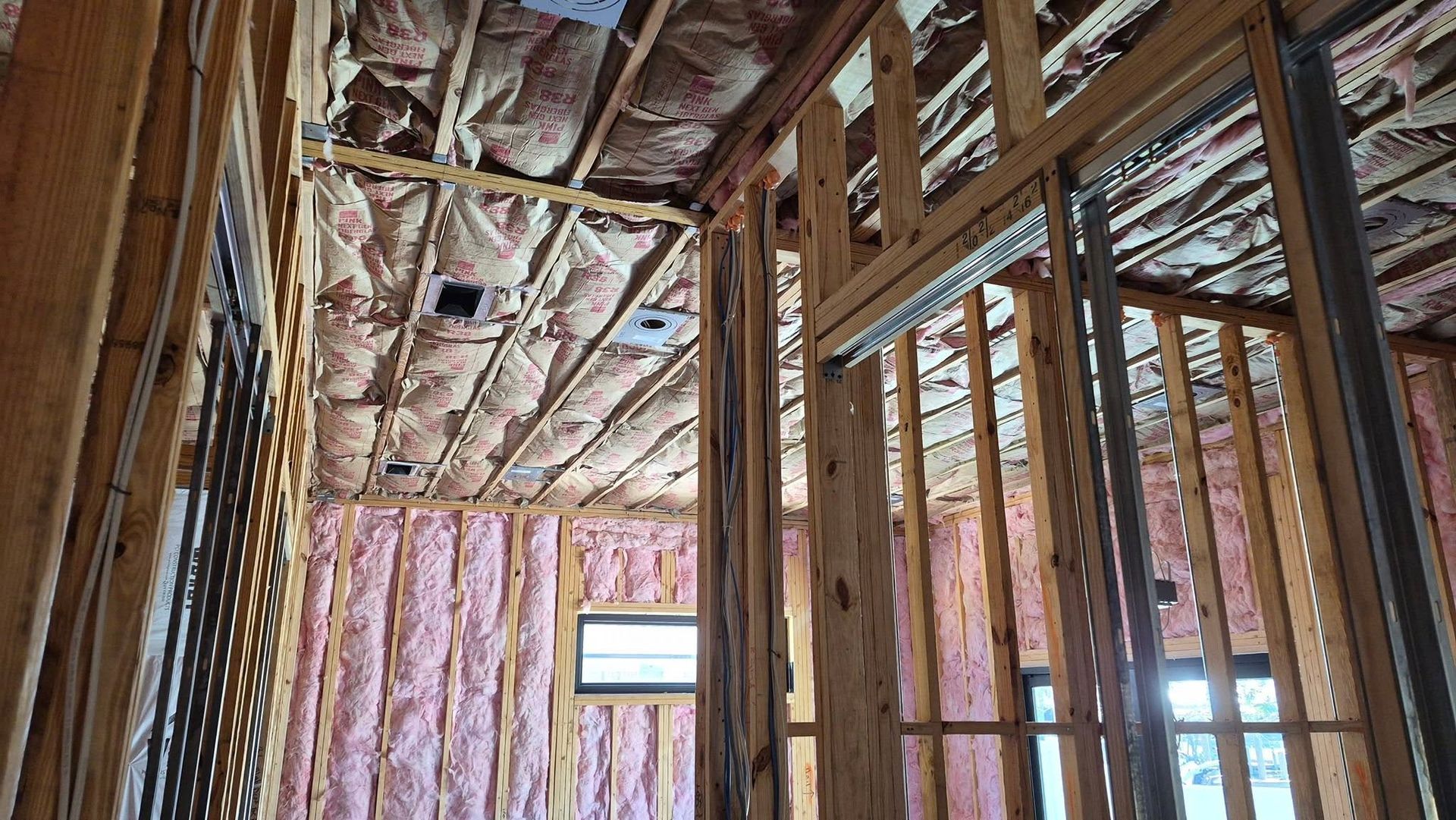 Interior of a house under construction with exposed wooden framing and pink insulation in the walls and ceiling.