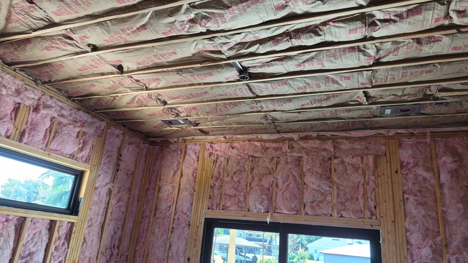 Insulated attic under construction with pink fiberglass in walls and unfinished ceiling joists