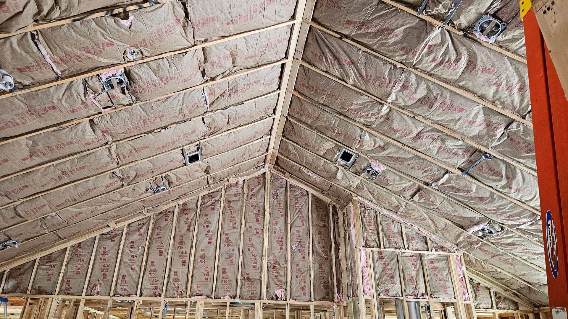 Insulated attic roof framing with exposed rafters and pink spray foam insulation panels