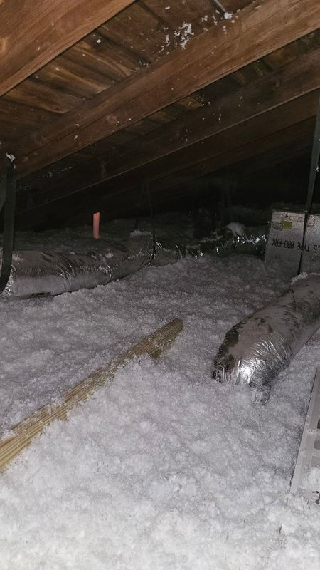 Snow-covered attic with exposed wooden beams and pipes, lit by a flashlight-like glow