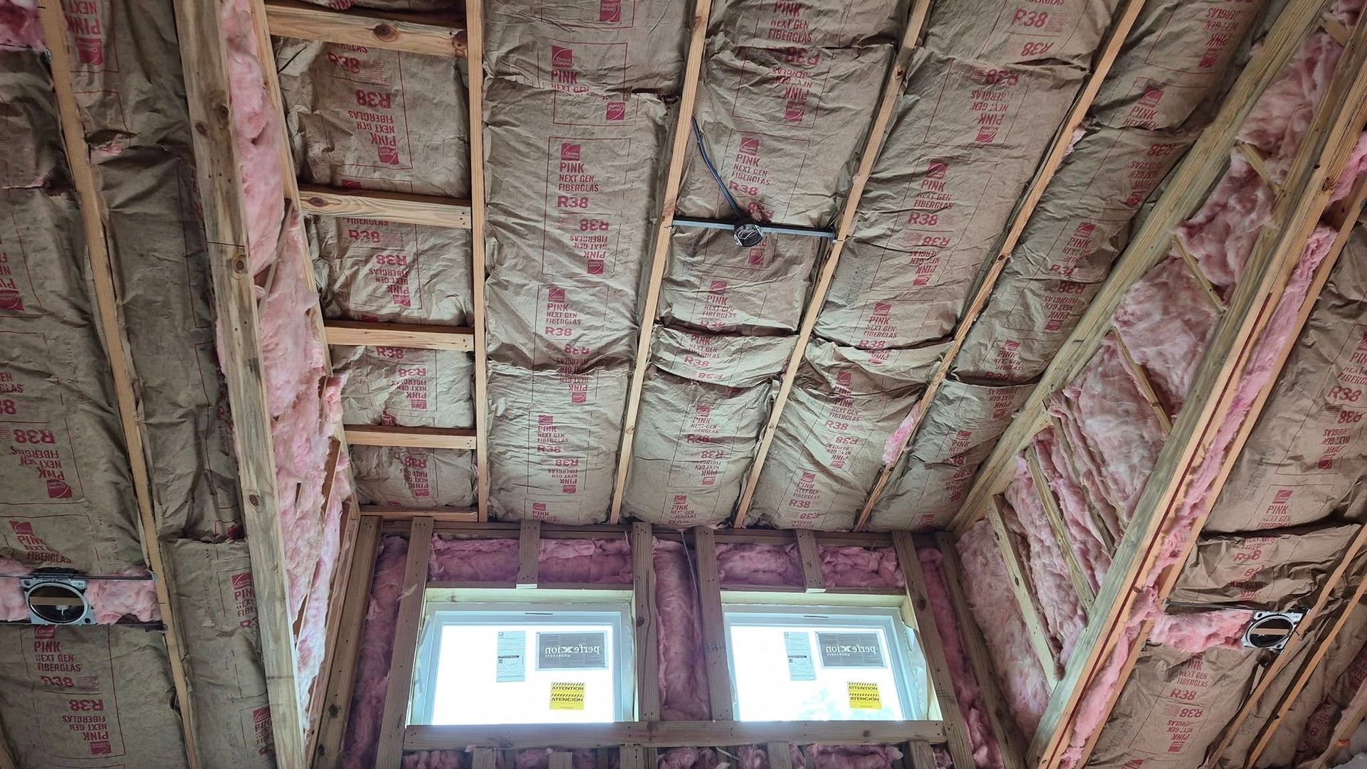 Exposed attic ceiling with pink insulation and two small windows at the far end